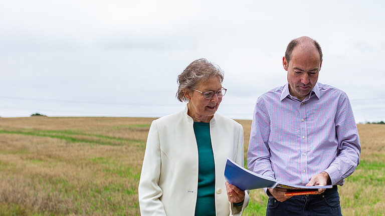 Councillors Janet Whitehouse and Jon Whitehouse study a map of the masterplan area standing in one of the masterplan area fields