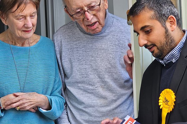 Rahim listening to the views of a man and a woman standing in the doorway of their home studying a leaflet