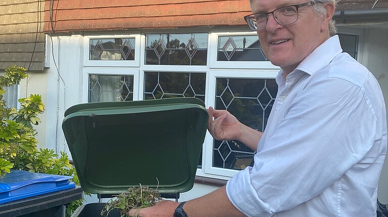 Edward Barnard in shirtsleeves putting garden rubbish into a green waste wheelie bin