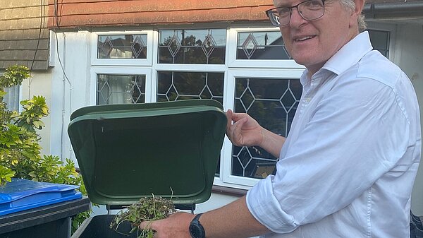 Edward Barnard in shirtsleeves putting garden waste into a green waste wheelie bin