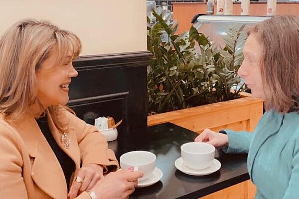 Razia Sharif and a resident sitting at a table discussing issues over cups of coffee