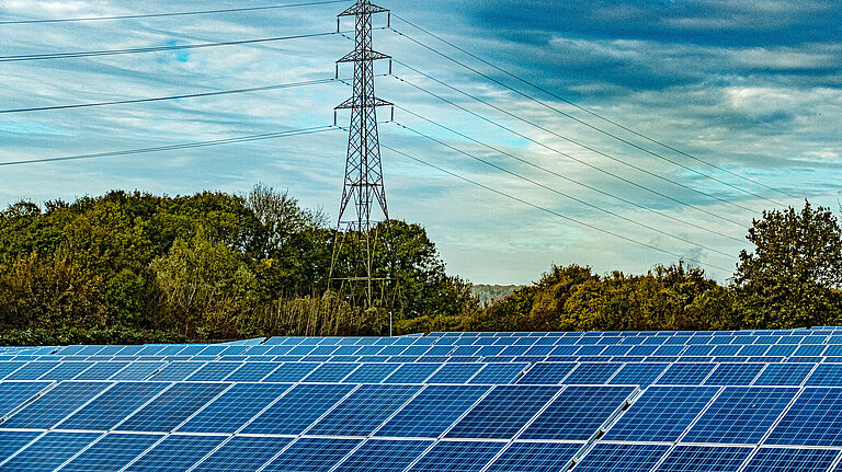 Solar panels with trees and electricity pylon on the background